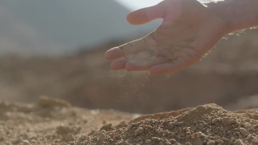 A close-up slow-motion shot of a person's hand letting dry, dusty earth sift through their fingers in an arid landscape