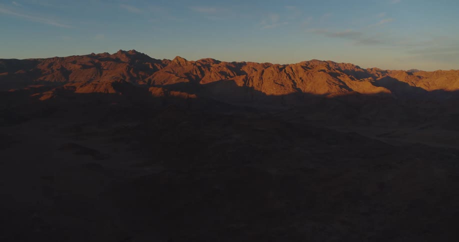 Static aerial shot of a majestic desert mountain range illuminated by the warm glow of a beautiful sunrise