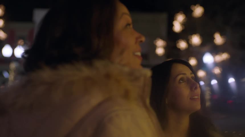 Two women looking up and talking on a city street at night