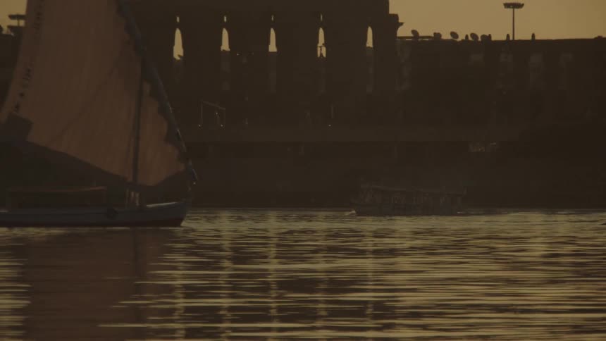 A traditional felucca sailboat peacefully sails along the Nile River in Luxor during a beautiful golden sunset