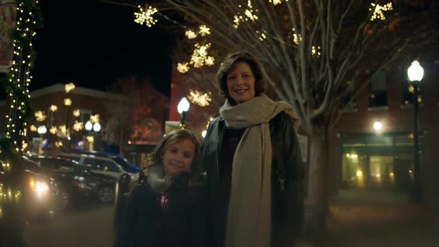 A woman and girl stand in front of christmas decorations in a city