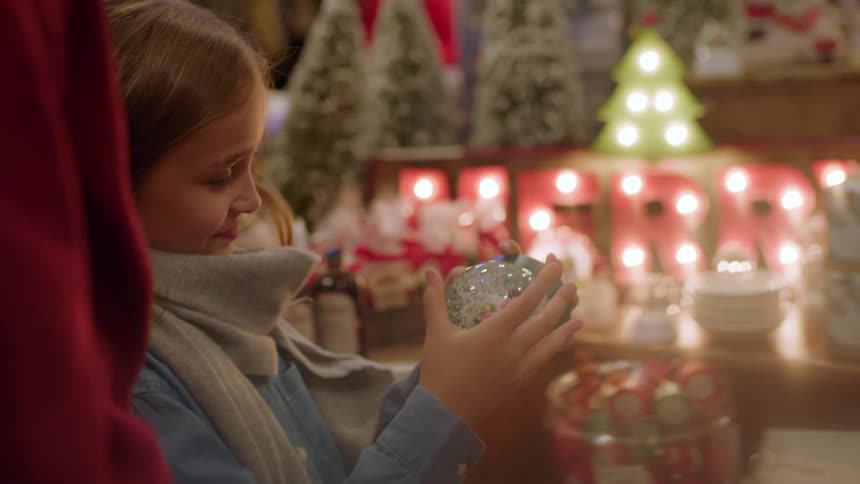 Woman hands little girl snow globe then little girl shakes it and smiles