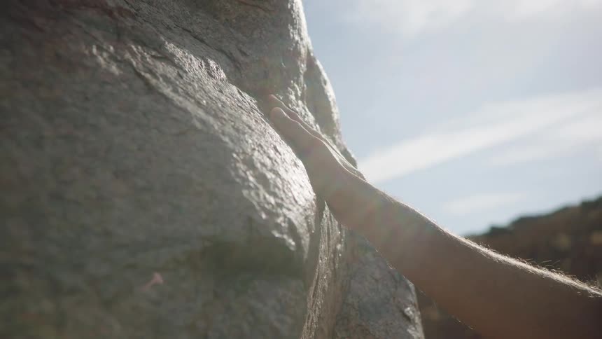 Close-up of a hand gently sliding down the surface of a large, sunlit rock
