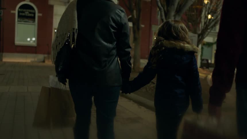 A family walks down the sidewalk at night talking
