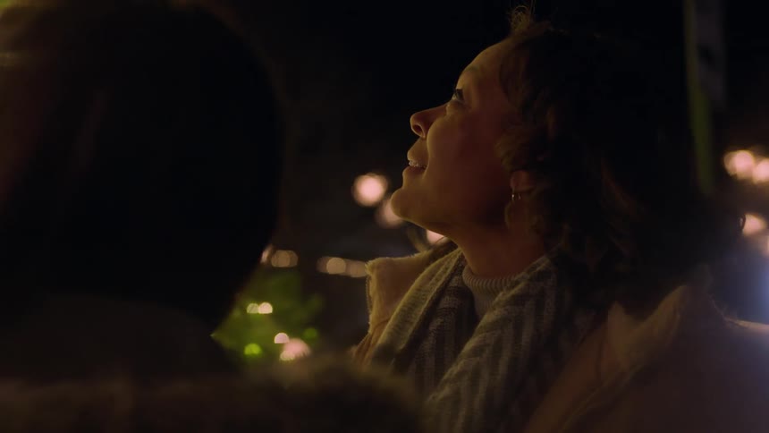 Two women talk at night in front of a christmas tree