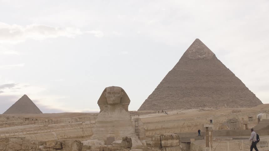 A static wide shot of the majestic Great Sphinx with the iconic Pyramids of Giza in the desert background