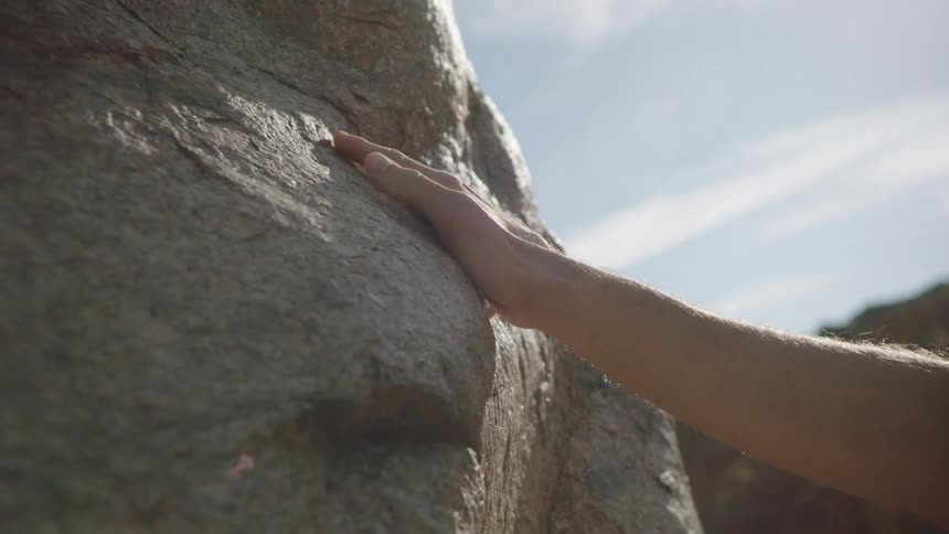 A gentle hand slowly glides over the sun-warmed, textured surface of a large rock in slow motion