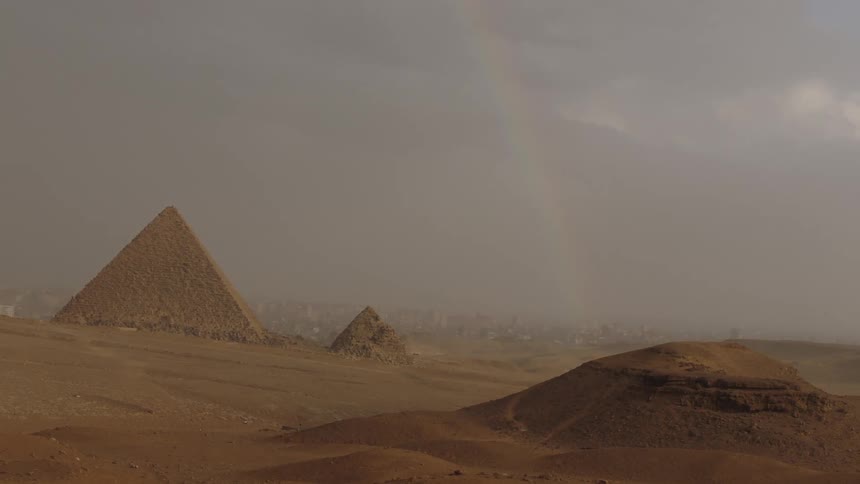 Stormy weather and a faint rainbow create a dramatic scene over the pyramids in the Egyptian desert