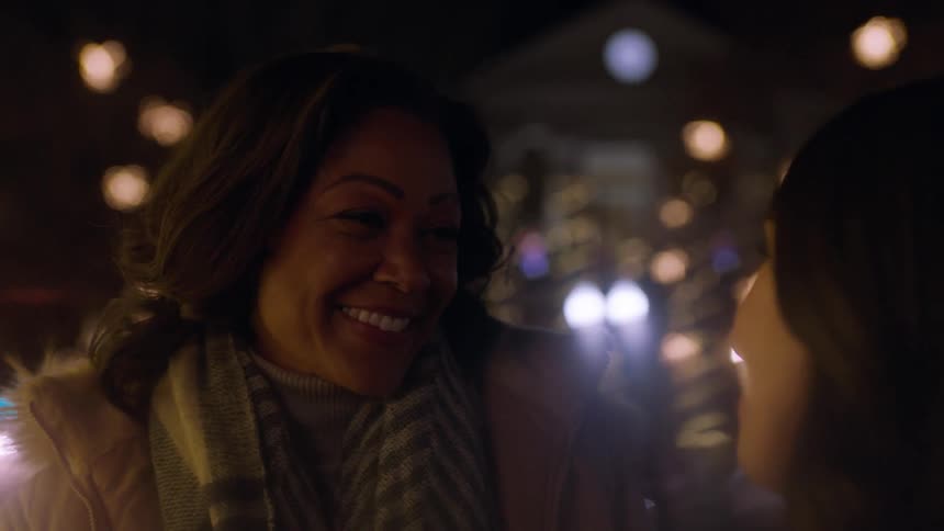 Two women staring up at christmas lights outside while talking and laughing
