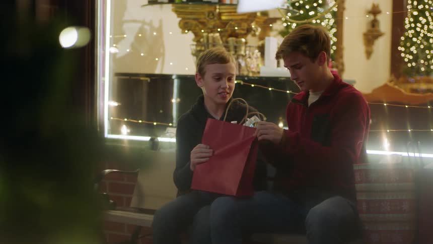 Boys sit on a city bench and fight over a shopping bag at christmastime