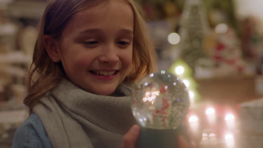 A girl smiles shaking a snow globe