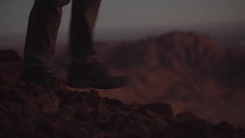 Slow motion close-up of a hiker's feet in boots walking along a rocky desert mountain path at twilight