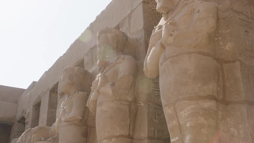 A low-angle shot of weathered ancient Egyptian statues lining a temple wall in the bright sun
