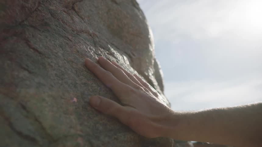 Slow motion close up of a hand gently touching and feeling the texture of a sunlit rock