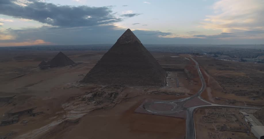 A stunning aerial view pulls back from the majestic Great Pyramid of Giza at dusk, revealing the vast desert landscape