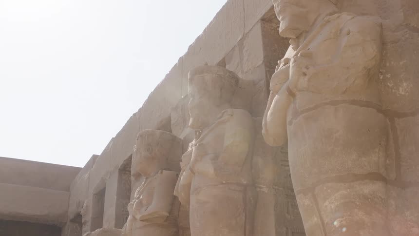 Sunlight beams across ancient weathered statues of pharaohs at an Egyptian temple