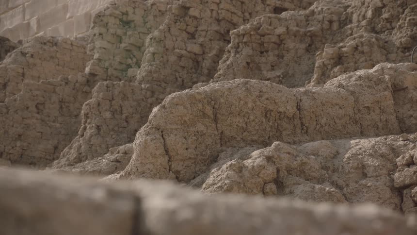 A slow zoom reveals the detailed texture of an ancient, crumbling mud-brick wall at an archaeological site