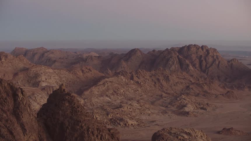 A stunning rack focus shot reveals the vast, rocky landscape of the Sinai desert mountains at sunrise