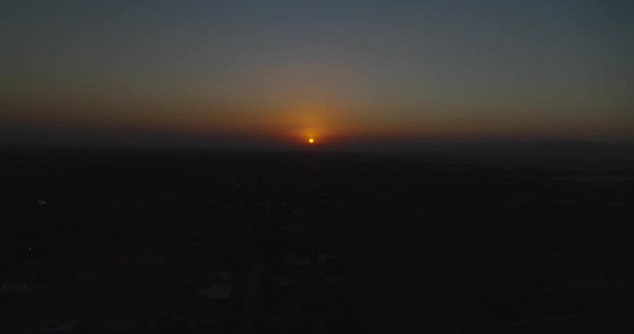 A stunning aerial view captures the vibrant sun setting on the horizon over a dark and quiet landscape