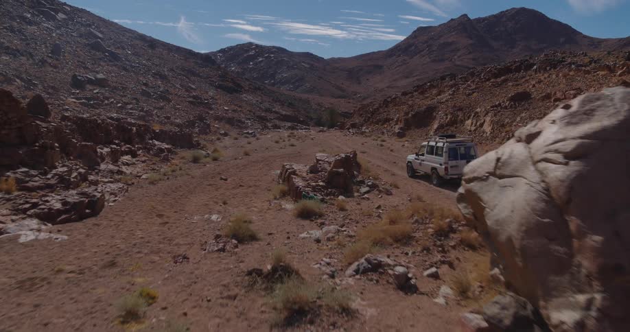 A slow aerial dolly shot moves towards a 4x4 off-road vehicle parked on a dirt track in a rugged desert mountain landscape