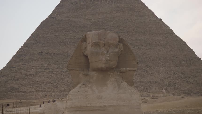 A camera tilts down from the sky to reveal the head of the Great Sphinx with the Great Pyramid of Giza in the background