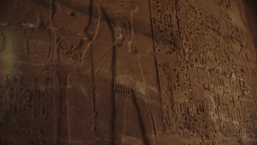 A slow upward pan of ancient Egyptian hieroglyphics and figures carved into a stone temple wall