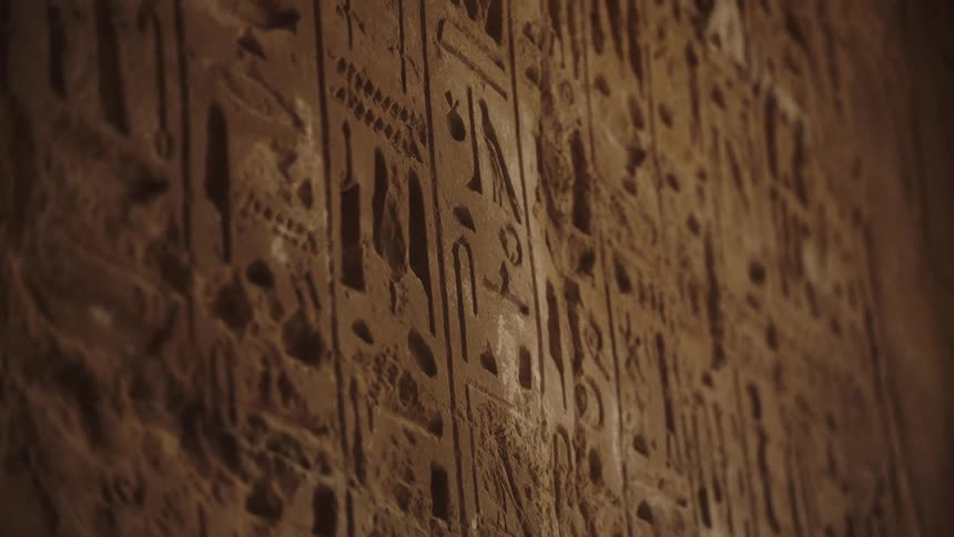 An atmospheric shallow depth of field shot reveals intricate details of ancient Egyptian hieroglyphics carved into a stone wall