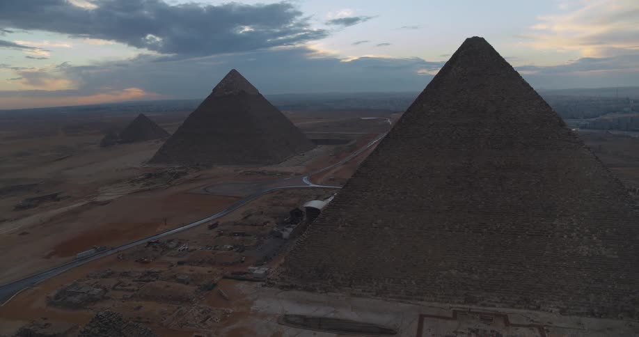 A majestic aerial view reveals the Great Pyramids of Giza standing tall against a cloudy sunset sky