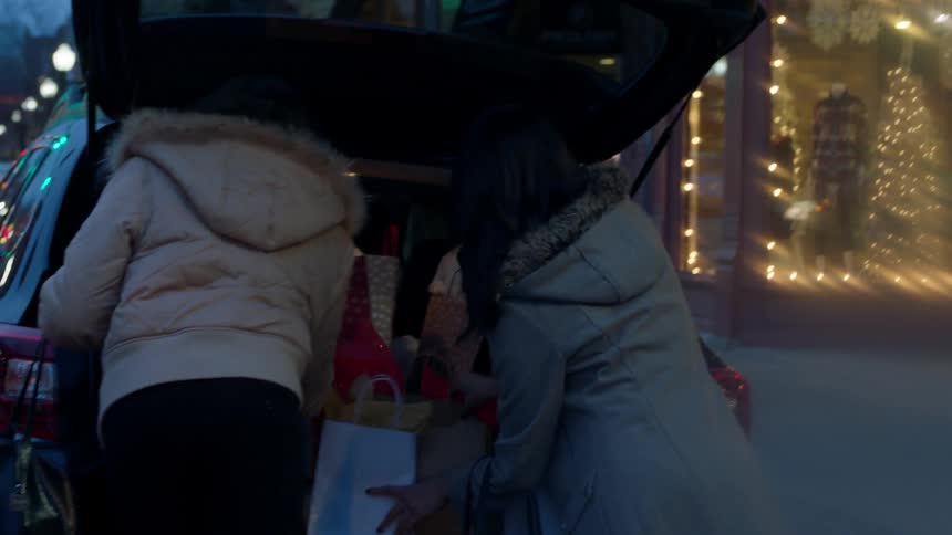 Two women open the trunk of a car and put bags in