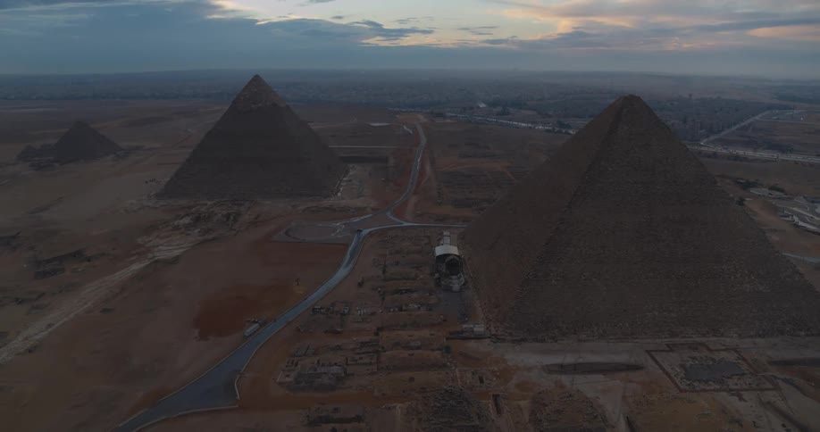 A majestic aerial view pulls back to reveal the Great Pyramids of Giza at dawn, showcasing their ancient grandeur against the vast Egyptian desert