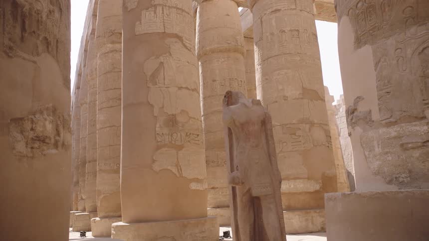 A headless ancient Egyptian statue stands among the massive hieroglyphic-covered columns of the Karnak Temple in Luxor, Egypt