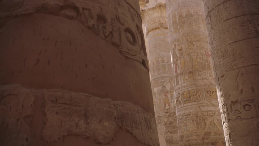 Sunlight illuminates the ancient Egyptian hieroglyphs carved and painted on the massive stone columns of a temple