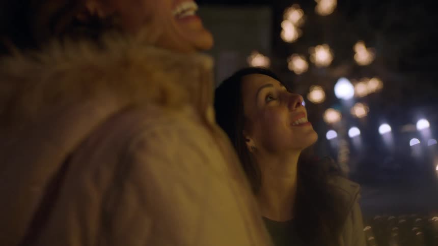 Two women talk and look at something at night