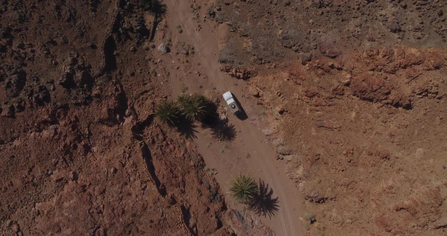 Ascending aerial shot reveals a white 4x4 truck driving and parking on a dirt track in a vast, arid canyon