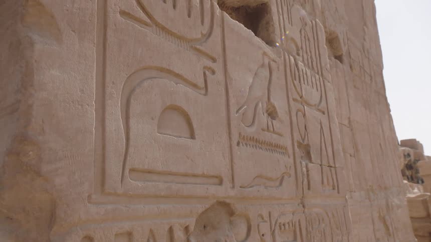 Close-up shot of ancient Egyptian hieroglyphs carved into a sunlit stone wall of a historic temple ruin