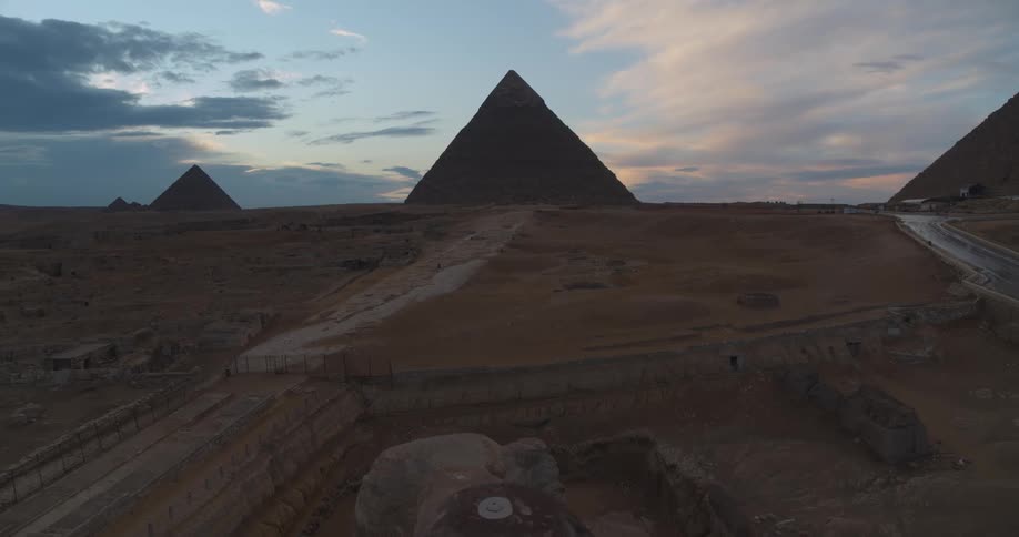 An epic aerial reveal of the Great Sphinx and the Pyramids of Giza silhouetted against a dramatic dusk sky