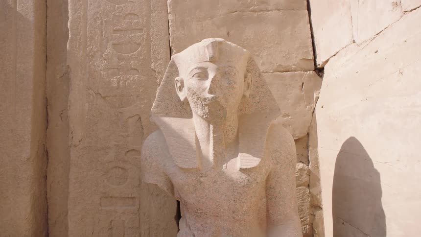 Time-lapse footage shows shadows moving across a weathered ancient Egyptian pharaoh statue at the Karnak Temple
