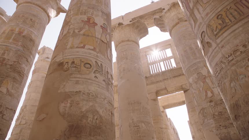 Sunlight streams through the massive, ancient columns covered in colorful hieroglyphics at the Karnak Temple in Luxor, Egypt