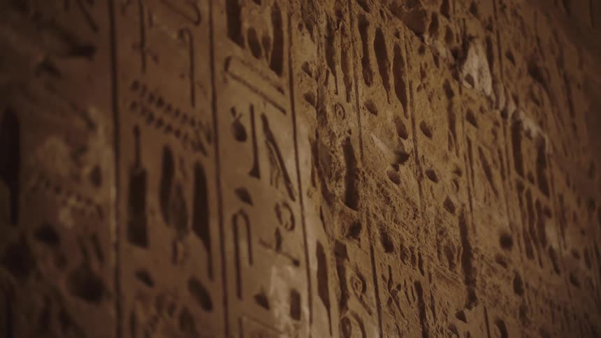 A close-up view of ancient Egyptian hieroglyphs carved into a stone wall slowly comes into focus