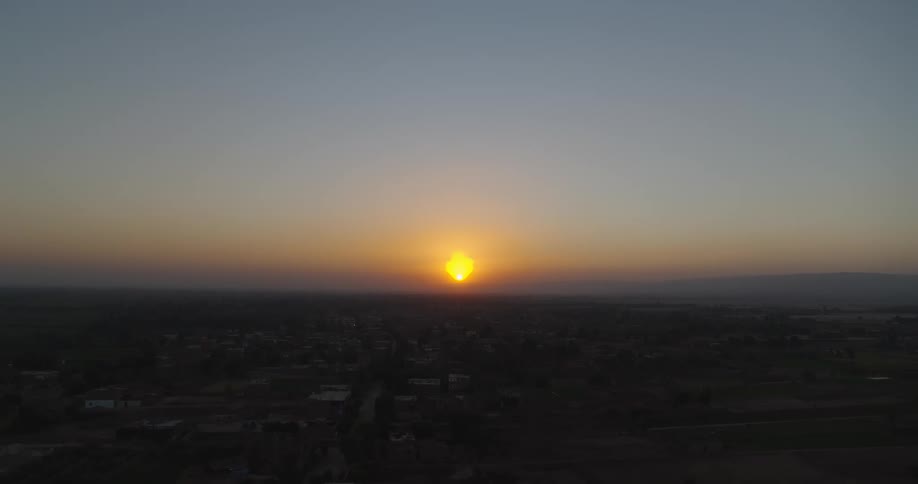 A slow aerial pullback reveals the golden sun setting over a peaceful rural village and the surrounding countryside