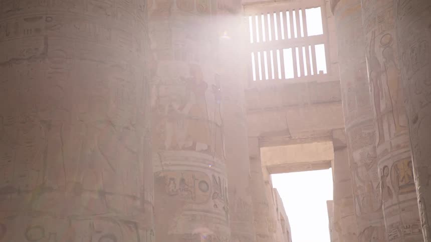 A slow reveal of towering ancient Egyptian columns covered in hieroglyphs as sunlight streams into the temple ruins