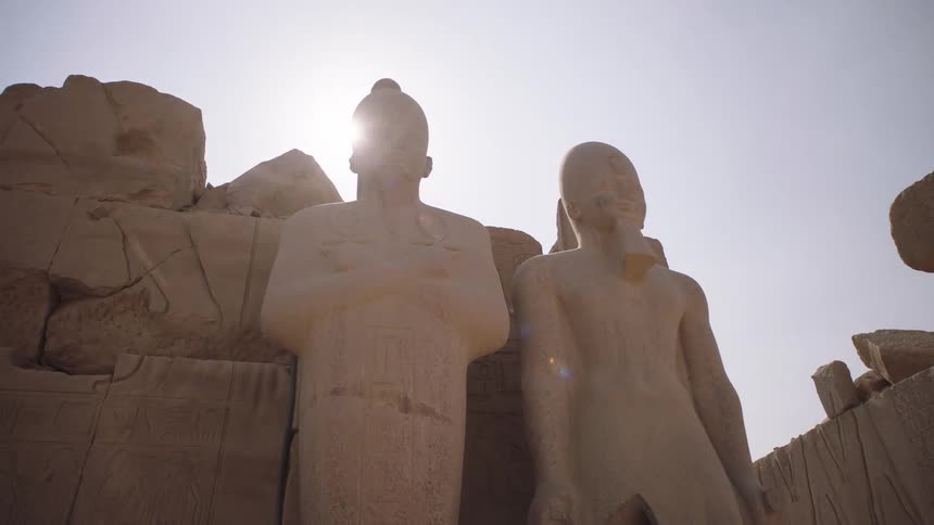 Majestic ancient Egyptian pharaoh statues stand silhouetted against the bright sun at a historic temple ruin