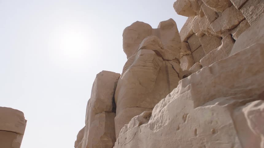 A slow-tracking shot reveals the massive, weathered stone ruins of an ancient Egyptian landmark under the bright sun