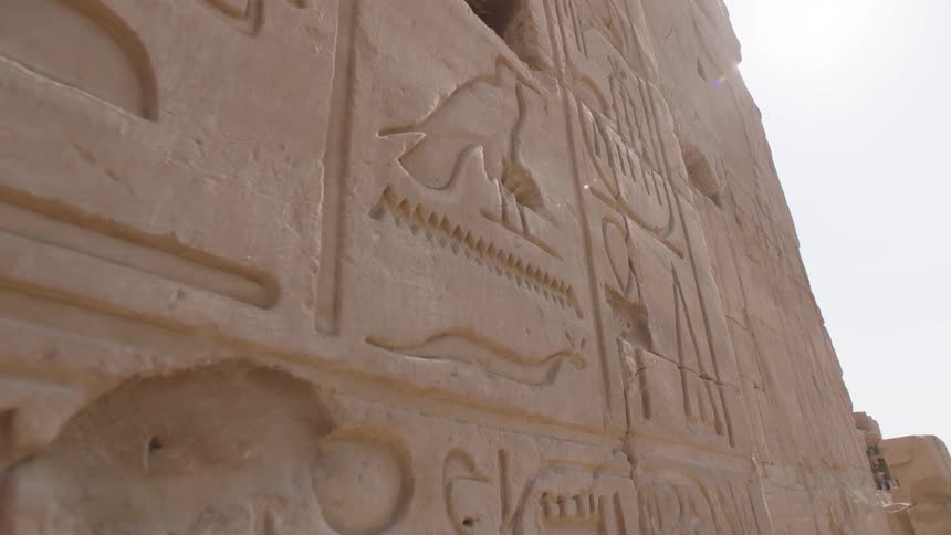 A slow dolly-out shot reveals ancient Egyptian hieroglyphic carvings on the sunlit stone walls of a temple ruin