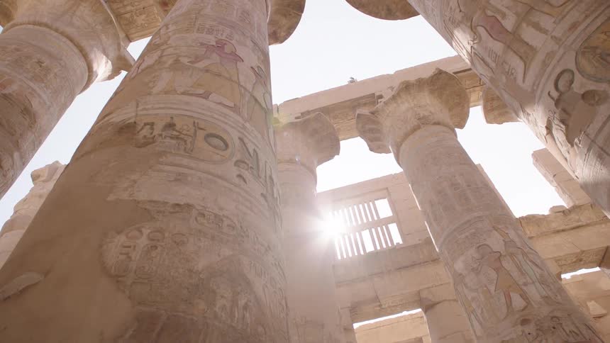 Sunlight beams through the grand, ancient columns decorated with hieroglyphics at the Karnak Temple in Egypt
