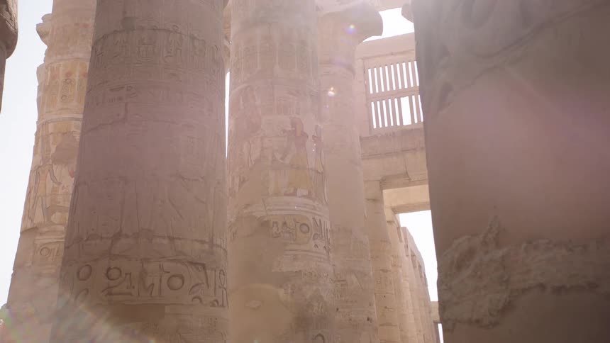 Sunlight flares through the massive, ancient Egyptian pillars covered in hieroglyphic carvings inside the Karnak Temple
