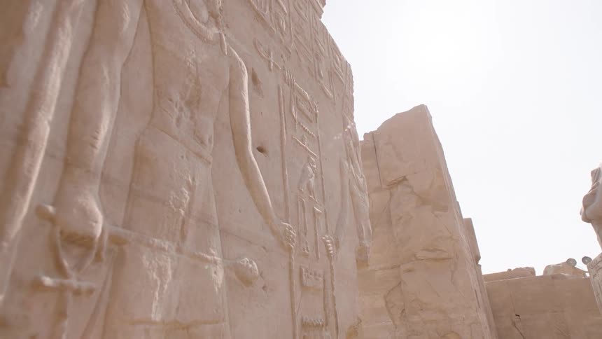 A slow tilt up an ancient Egyptian temple wall reveals intricate hieroglyphics and carvings illuminated by the bright desert sun
