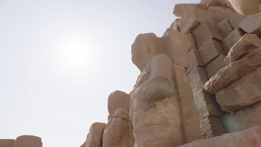 A low-angle pull-back shot reveals a row of ancient Egyptian pharaoh statues at the Karnak Temple under the bright sun