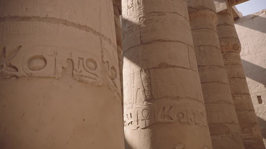A slow-moving shot reveals ancient Egyptian hieroglyphs carved into the massive stone columns of the Karnak Temple