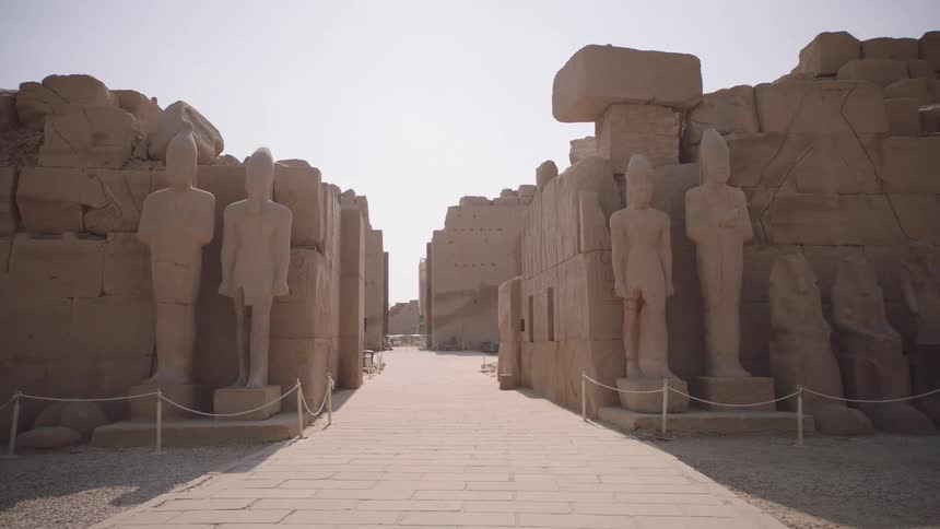 A slow pullback shot reveals towering ancient Egyptian pharaoh statues lining a sun-drenched pathway within a historic temple complex